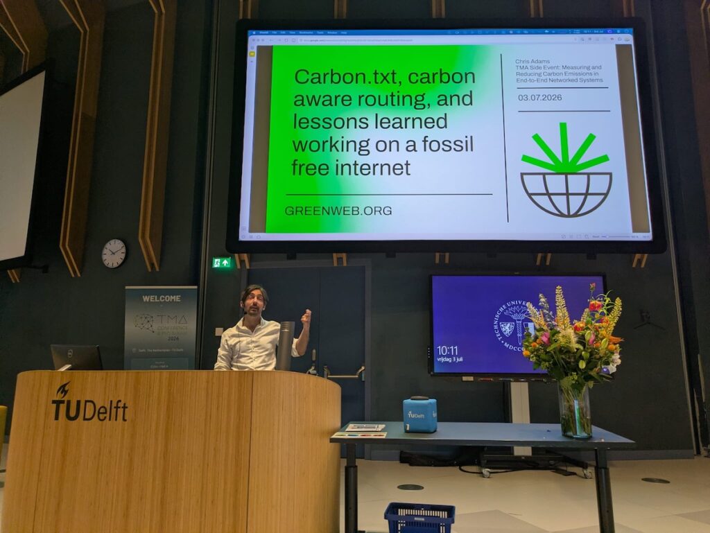 Chris Adams standing on a stage, with a screen behind saying "Carbon.txt, carbon aware routing, and lessons learned working on a fossile free internet
