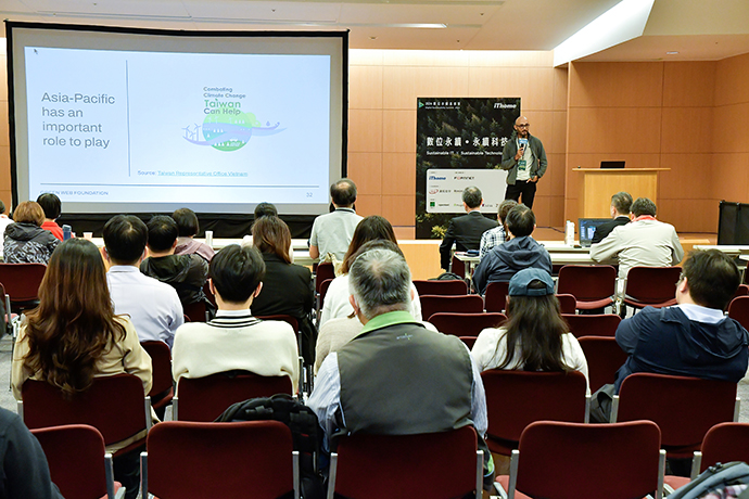 Audience members watching a man standing on stage with a microphone presenting a slide which reads "Asia-Pacific has an important role to play". A graphic on the slide reads "Combating Climate Change, Taiwan Can Help".