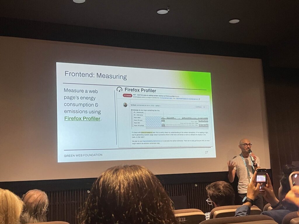 A slide from my presentation talking about the Firefox Profiler. It reads - "Frontend: Measuring - Measure a web page's energy consumption and emissions using Firefox Profiler". A man with a microphone is standing to the right of the slide speak to the audience.