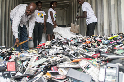 Four people shoveling a large pile of old phones into bags.